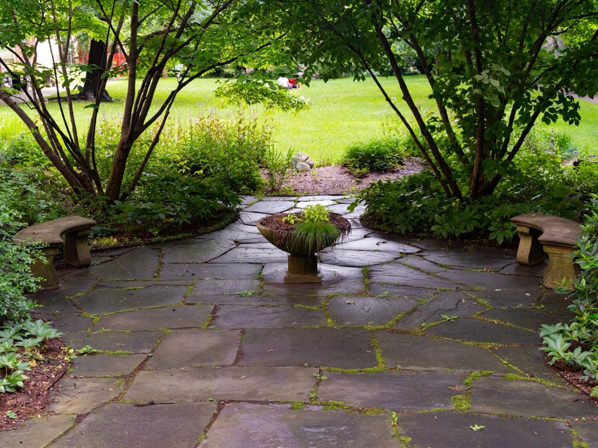 Flagstone patio framed by mature plantings and stone benches