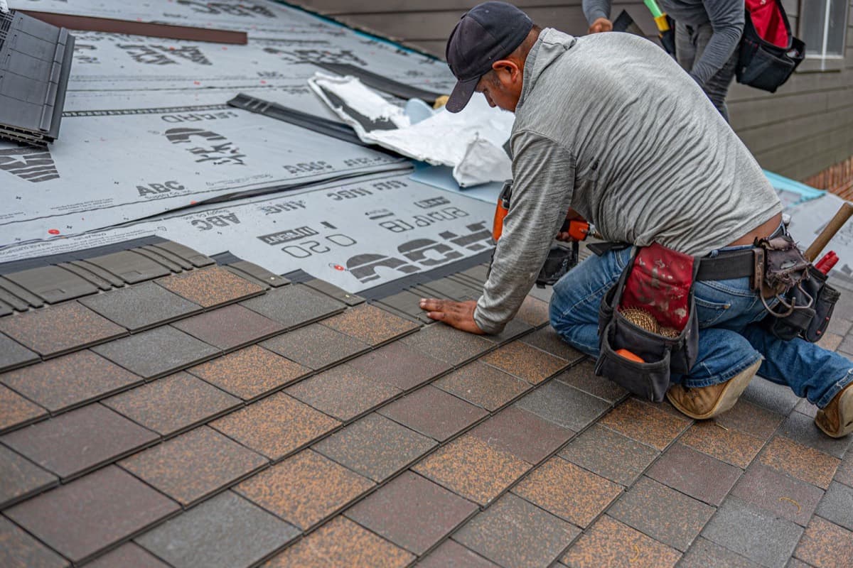 Roofer laying new architectural shingles over fresh underlayment